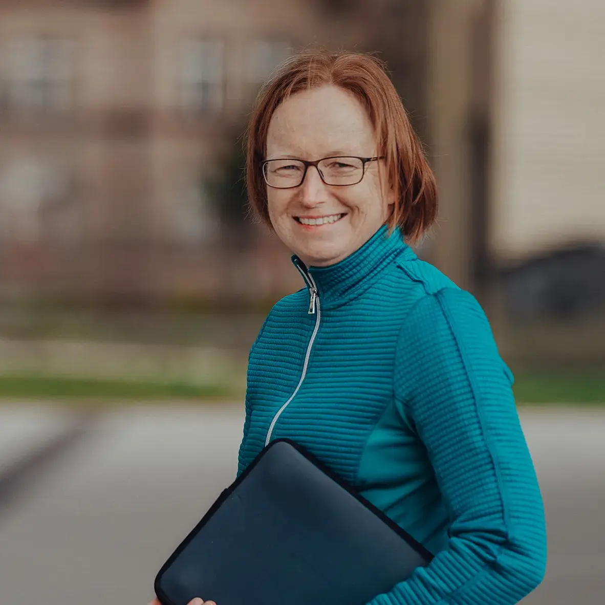 Christina bei wir unterwegs, im Produktmanagement & Sales tätig, steht mit einem Lächeln und einer Laptoptasche im Arm im Freien – sie sorgt für reibungslose Abläufe bei Gruppenreisen und Teamevents.