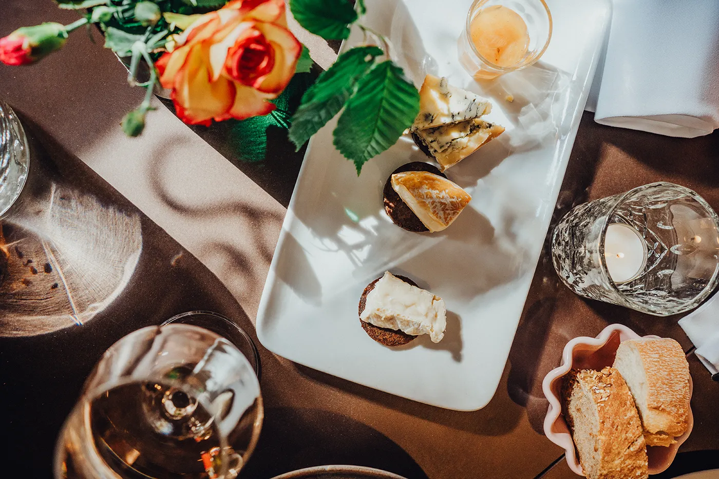 Nahaufnahme eines gedeckten Tisches mit Käseauswahl, Brot, Wein und einer Blume – stimmungsvolle Szene eines kulinarischen Highlights während einer intensiven Gruppenreise oder eines Teamevents.