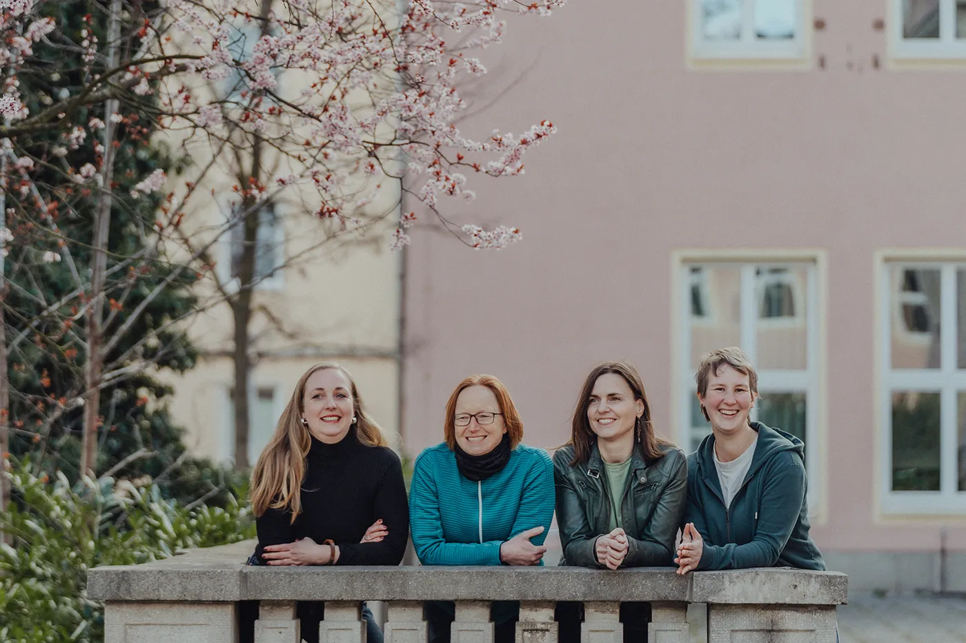 Das Team von wir unterwegs steht lächelnd unter blühenden Bäumen und blickt in die Kamera – die Expertinnen für intensive Gruppenreisen und kreative Teamevents.