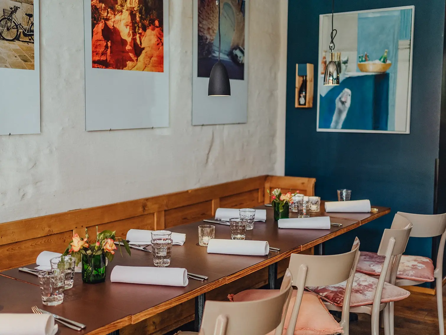 Gedeckter Holztisch im Ballenberger Restaurant in Erfurt mit Gläsern, Stoffservietten, Blumenvasen und Wandkunst im Hintergrund, einladendes Ambiente für Gruppen und Teams.