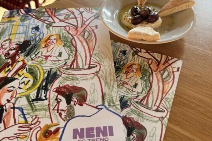 Ausschnitt vom Tisch im Restaurant Neni mit kunstvoll gestalteter Speisekarte und einem kleinen Vorspeisenteller mit Brot, Oliven und Dip.